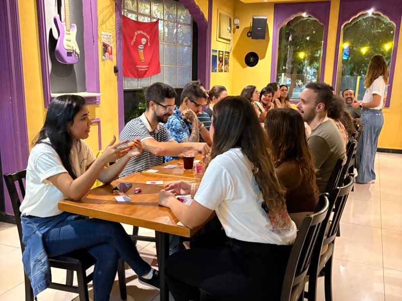 Participantes conversando ao redor da mesa comprida, com a bandeira do Copo pendurada na parede amarela.
